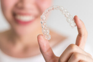 A smiling woman holding invisalign or invisible braces, orthodontic equipment For You Dental in Carrollton, TX